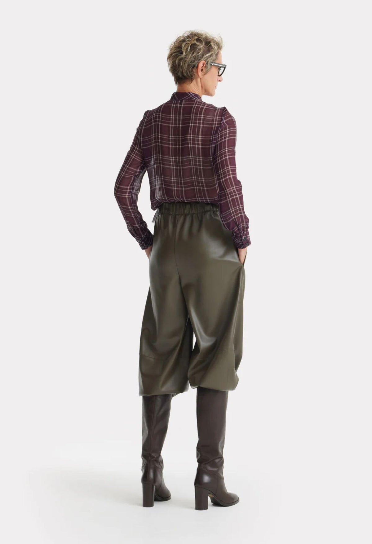 Person wearing a plaid shirt, green wide-leg pants, and brown boots on a white background