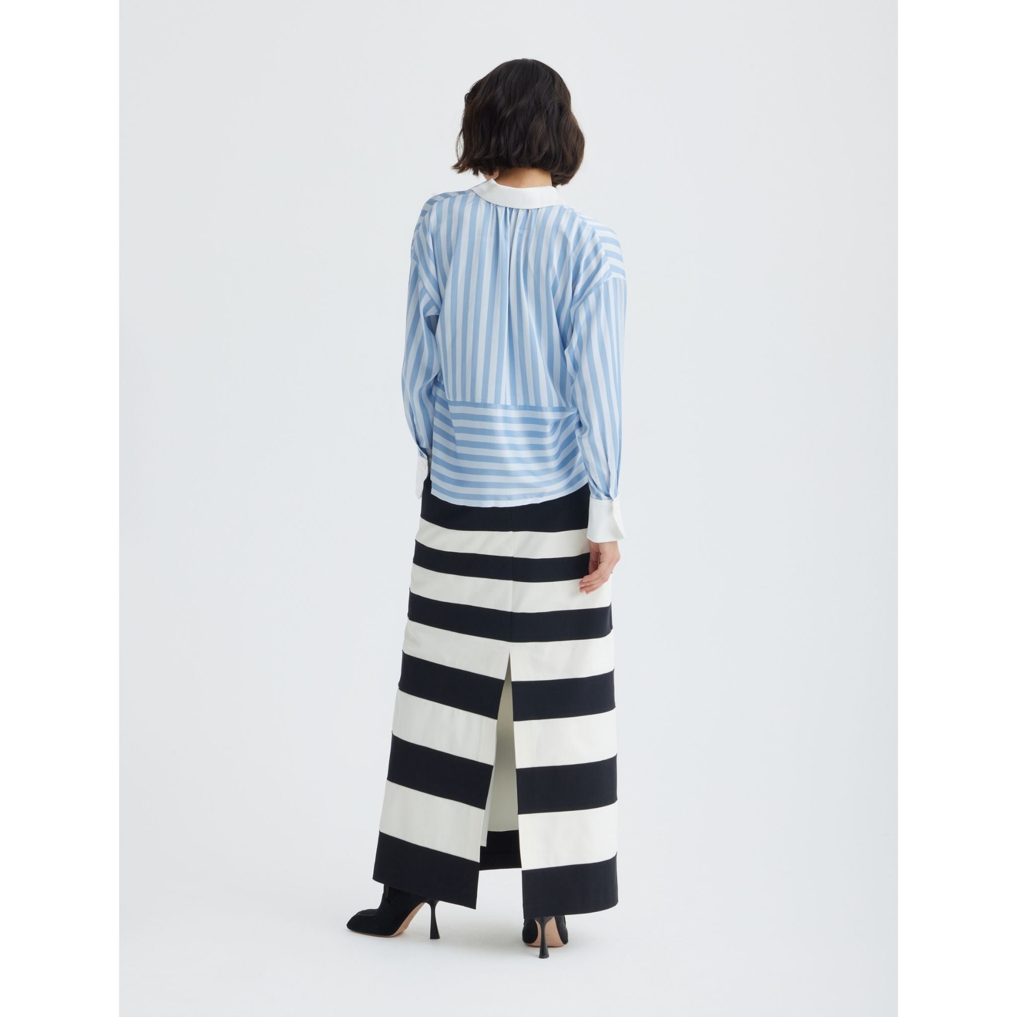 A woman is seen from behind wearing the JULIA ALLERT Smart Elegance Silk-Touch Striped Long-Sleeve Blouse in light blue, featuring an oversized white collar paired with a black and white striped maxi skirt.