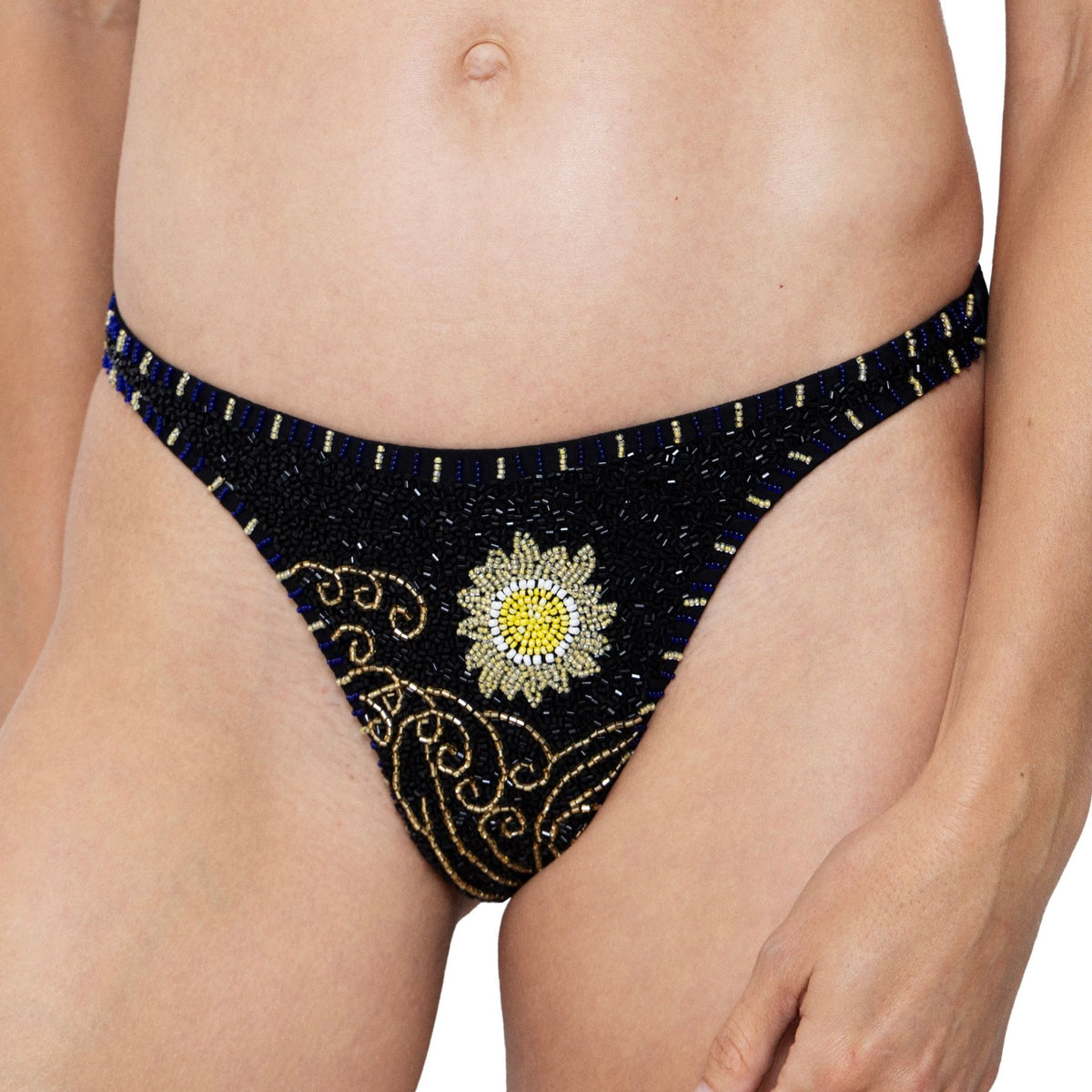 The SELF-ADORE Dark Tide Hand-Beaded Embellished Bikini Bottom in black features gold and blue patterns with a central yellow and white embroidered flower for a striking swimwear look.
