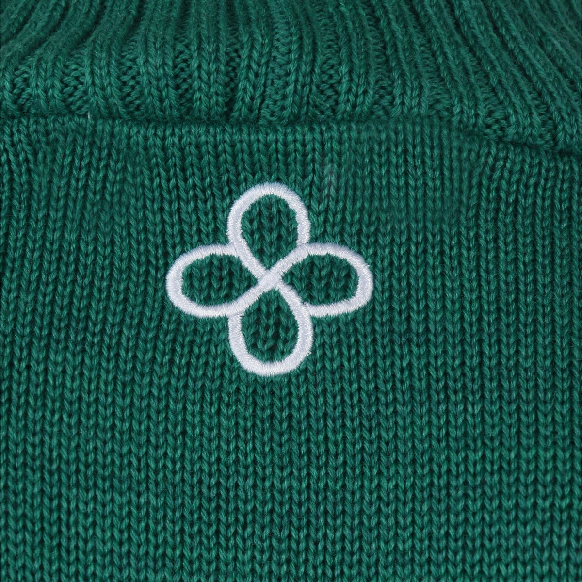 Green knitted fabric with a white embroidered four-leaf clover design.