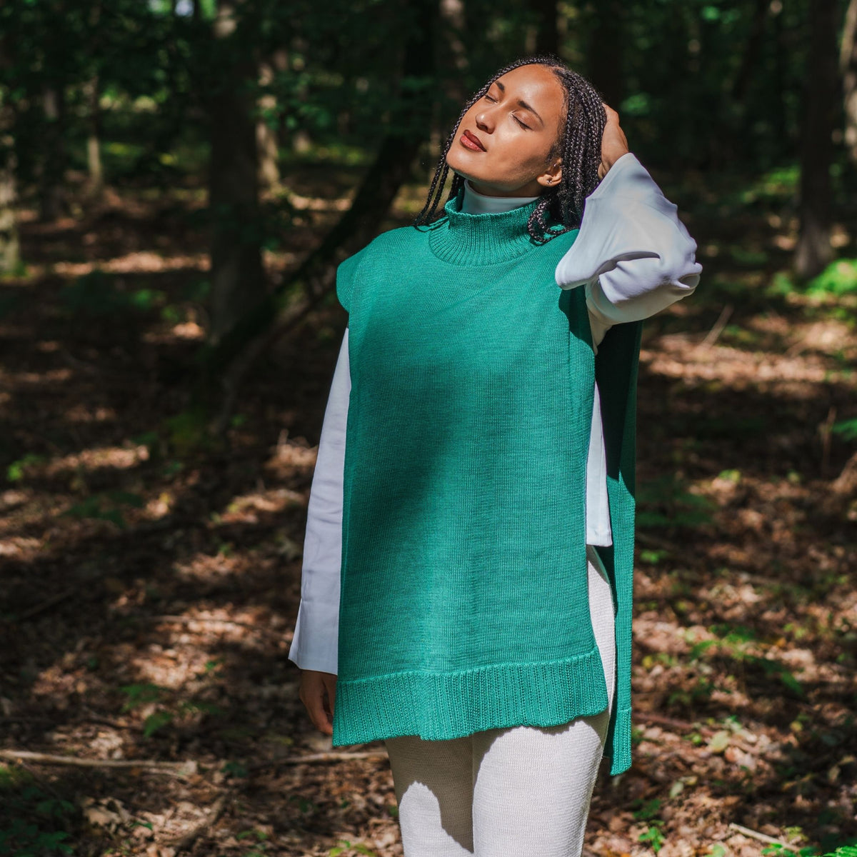Person wearing a teal sweater over a white shirt in a forest setting