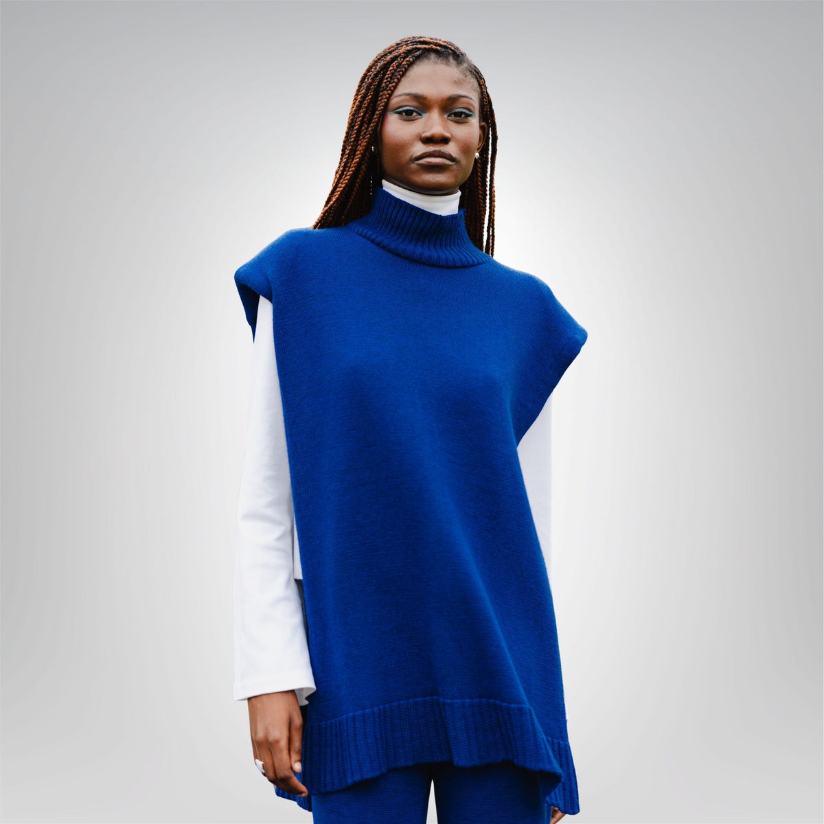 Woman wearing a blue sleeveless sweater over a white shirt on a gray background