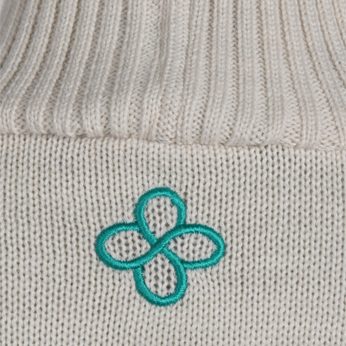 Close-up of a gray knit fabric with a teal embroidered flower design.