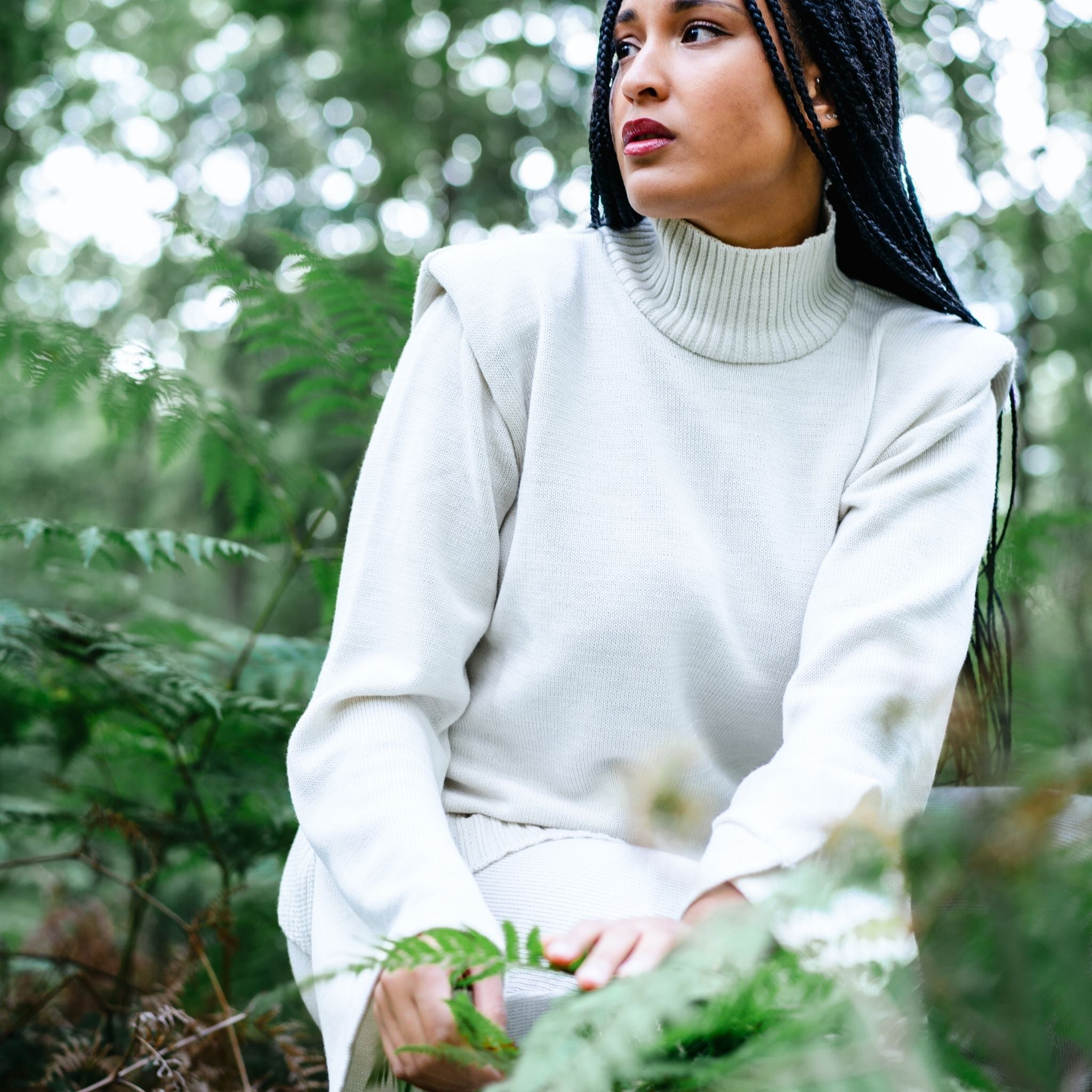Woman in a white turtleneck sweater sitting among green foliage
