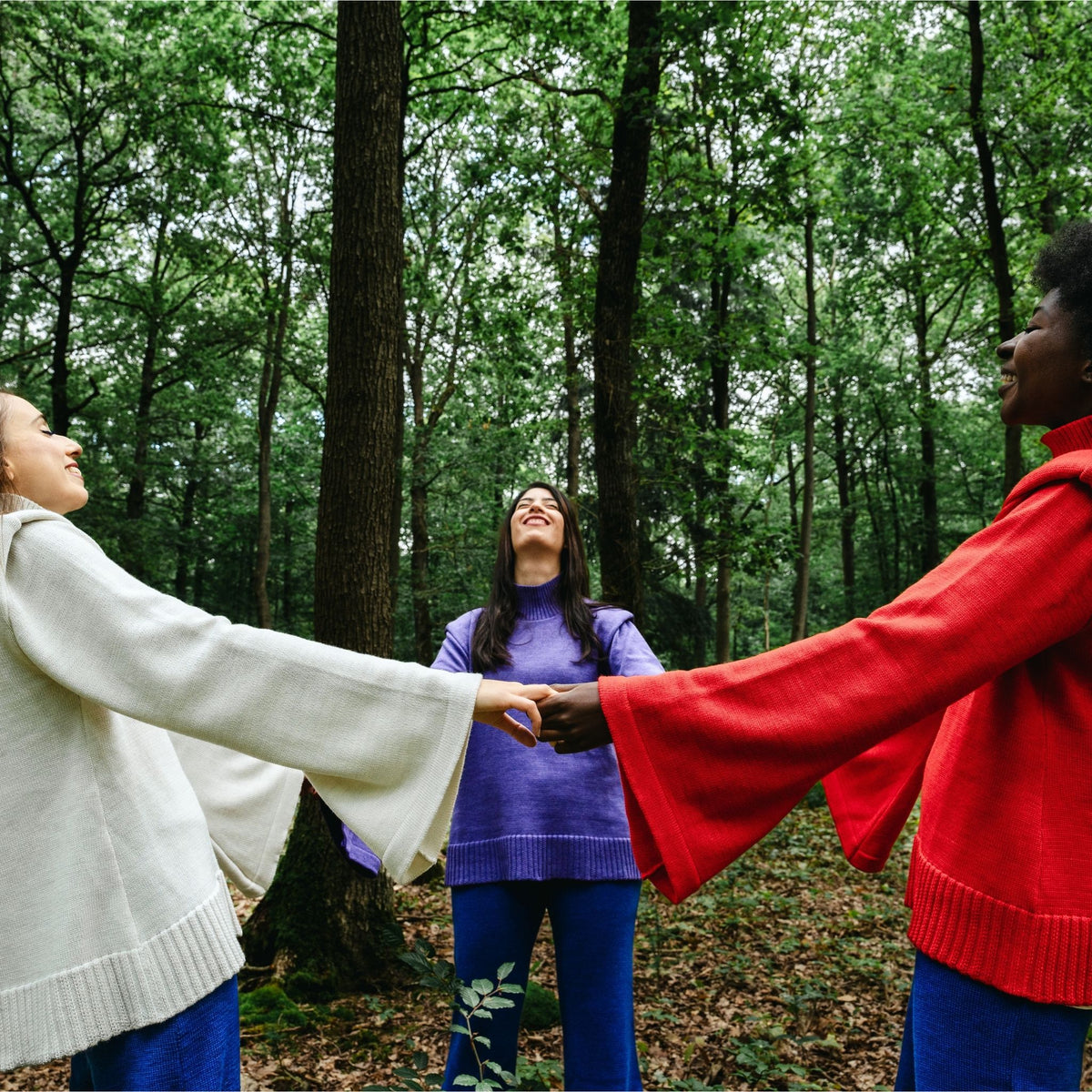Three people holding hands in a circle in a forest