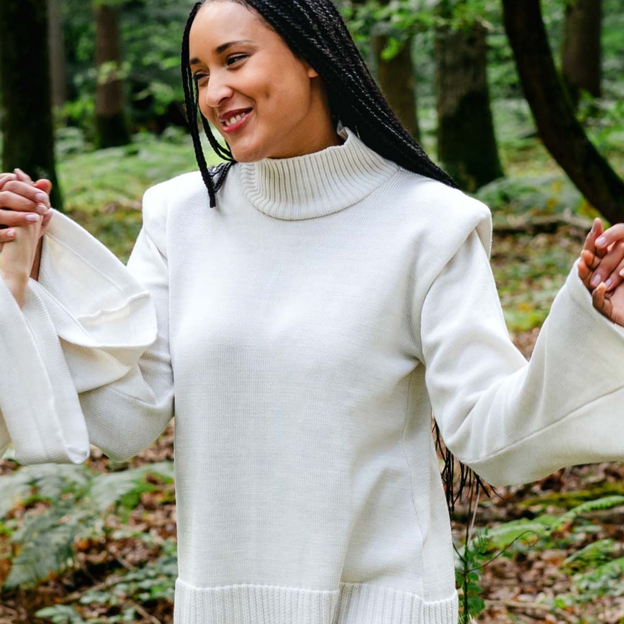 Woman in a white sweater holding hands with another person in a forest setting