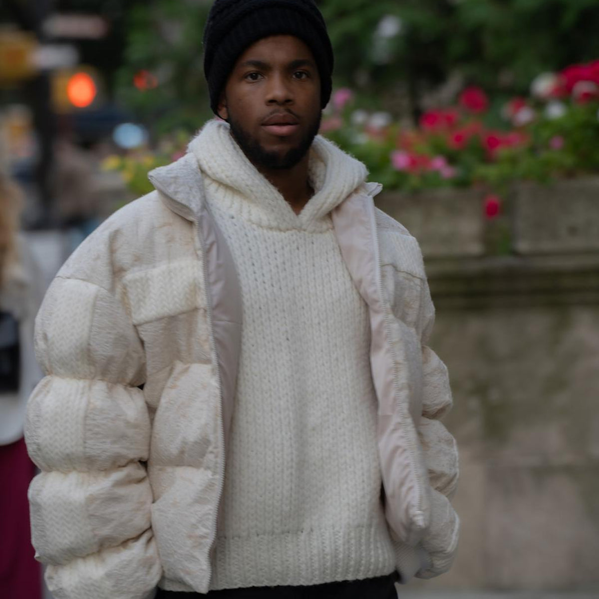 Man wearing a cream puffer jacket over a white sweater with a blurred background