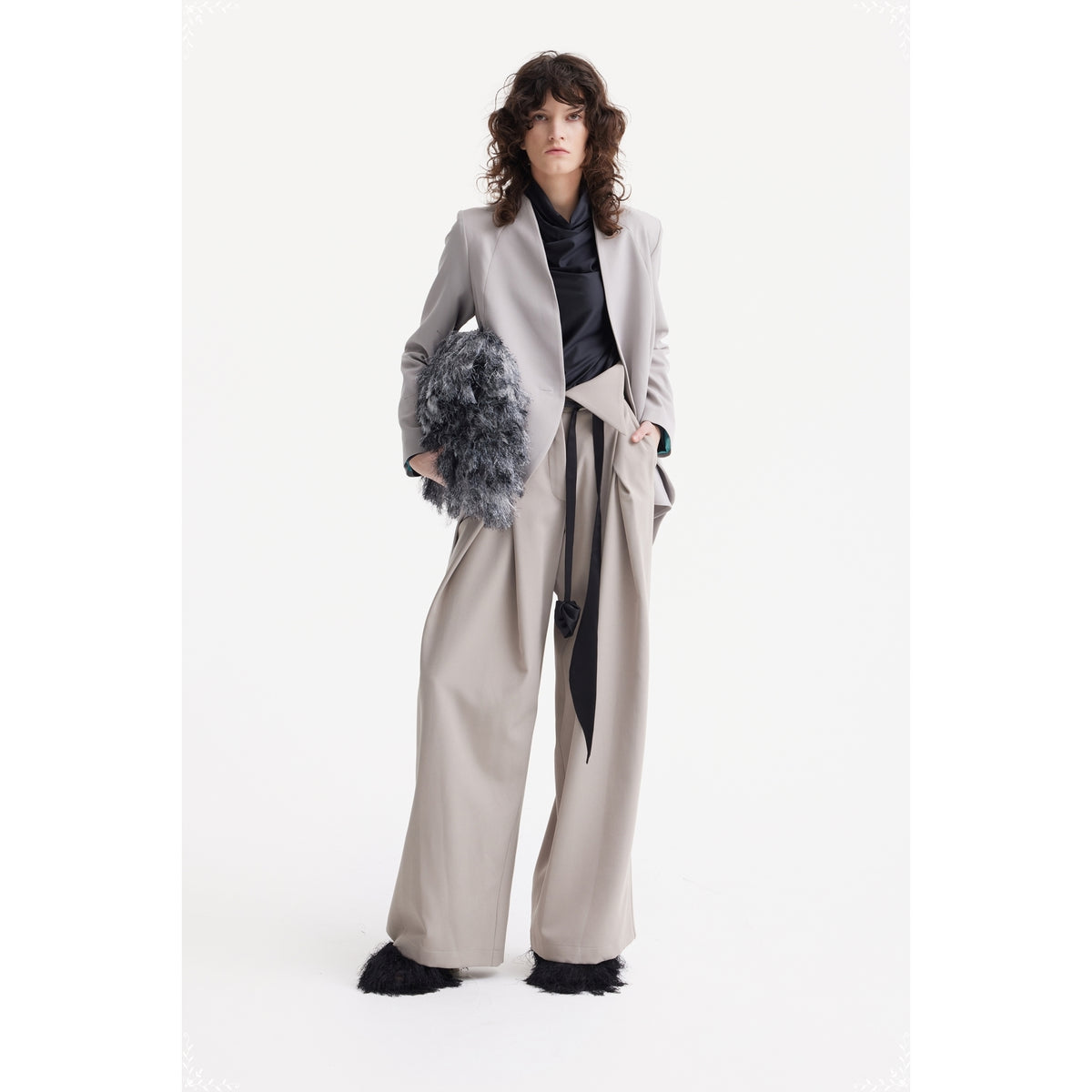 A woman with wavy hair wears the JULIA ALLERT Fashion Forward Wide-Leg Pants &amp; Contrast Belt in beige, a light gray blazer, black top, and black furry shoes. She holds a fluffy gray handbag against a plain white background.