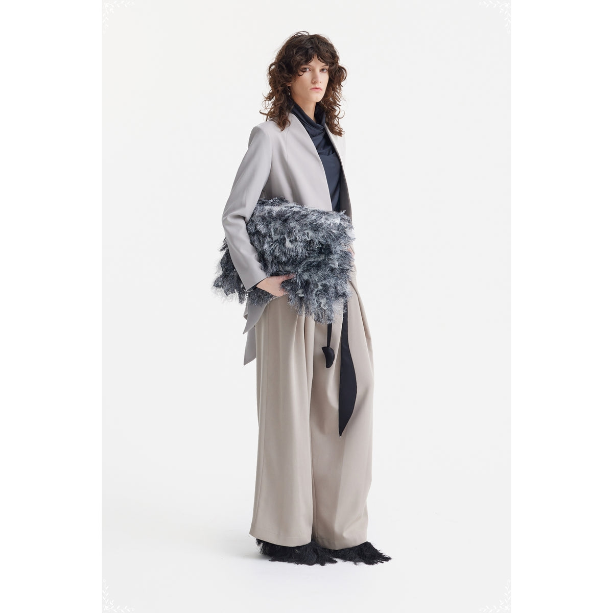 A woman with wavy brown hair wears JULIA ALLERT's Fashion Forward Wide-Leg Pants &amp; Contrast Belt in beige, pairing them with a dark top and holding a large textured clutch, standing against a plain white background.