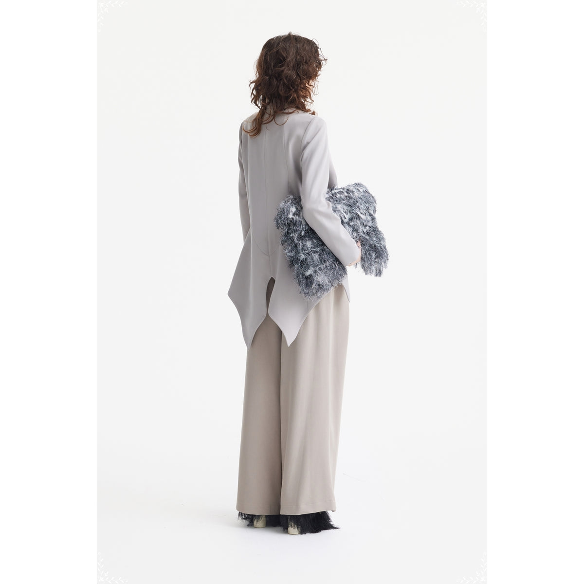Seen from behind against a plain white background, a person with curly hair wears JULIA ALLERT’s Fashion Forward Wide-Leg Pants &amp; Contrast Belt in beige and a light gray tailored jacket, holding a textured, fluffy gray accessory.