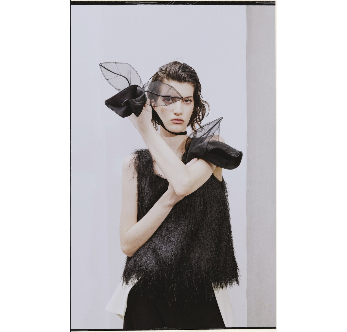 A woman wearing the JULIA ALLERT Fringe Sleeveless Top in black poses with one arm raised, dramatic black bows with sheer fabric on her wrists, set against a plain, light background.