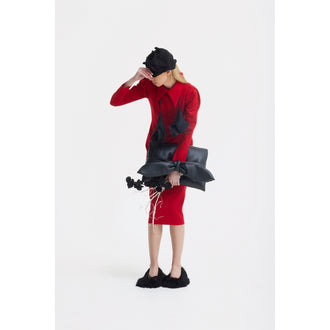 Wearing a JULIA ALLERT Solid Formal Midi Dress in red and a black hat, a person stands against a white background holding black sculptural objects and dried flowers. They wear black furry shoes and partially cover their face with one hand.