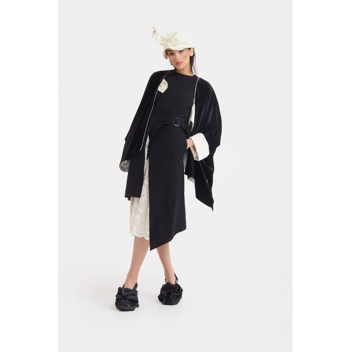 A woman models the JULIA ALLERT Loose Velvet Cape Jacket With Zip Front in black, styled with a belted skirt, lace hem, bow-detailed shoes, and a white headscarf—an elegant evening look set against a plain white background.