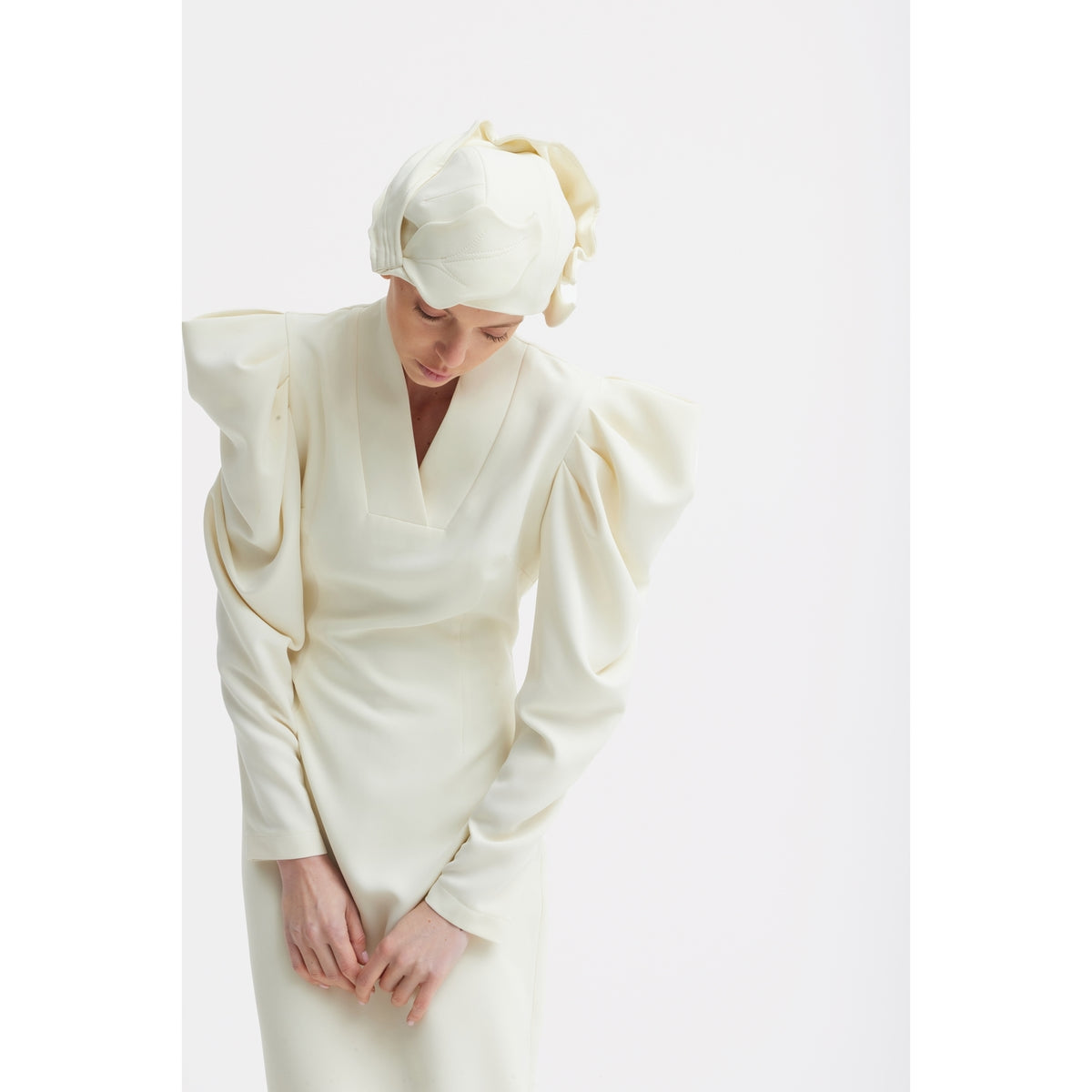A person wears the JULIA ALLERT Crepe Midi Dress With Statement Sleeves in Ivory, paired with a matching headscarf, standing against a plain white background and looking down with hands gently clasped.