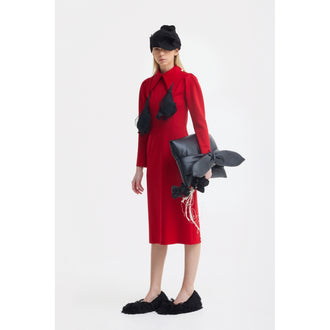 A woman in a JULIA ALLERT Solid Formal Midi Dress - Red, black furry slippers, a black headpiece, and a sculptural black bow-accented bag stands against a plain white background.