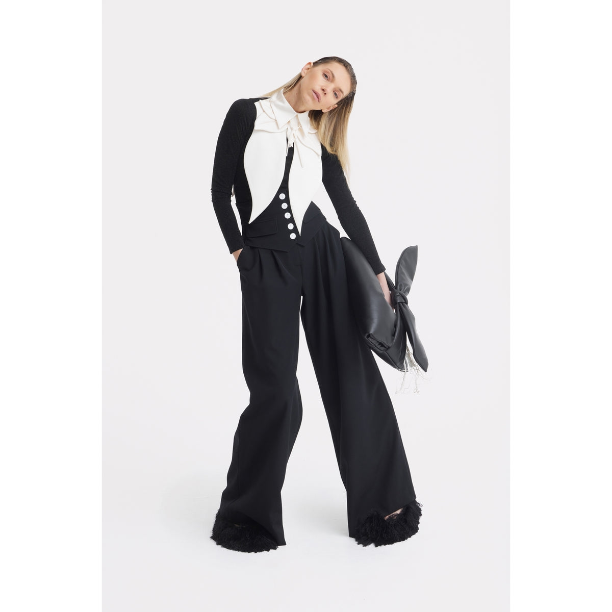 A woman models JULIA ALLERT’s Buttoned Corset-Waist Black Tailored Trousers with a white vest over a black long-sleeve top and a large black handbag, standing against a plain white background.