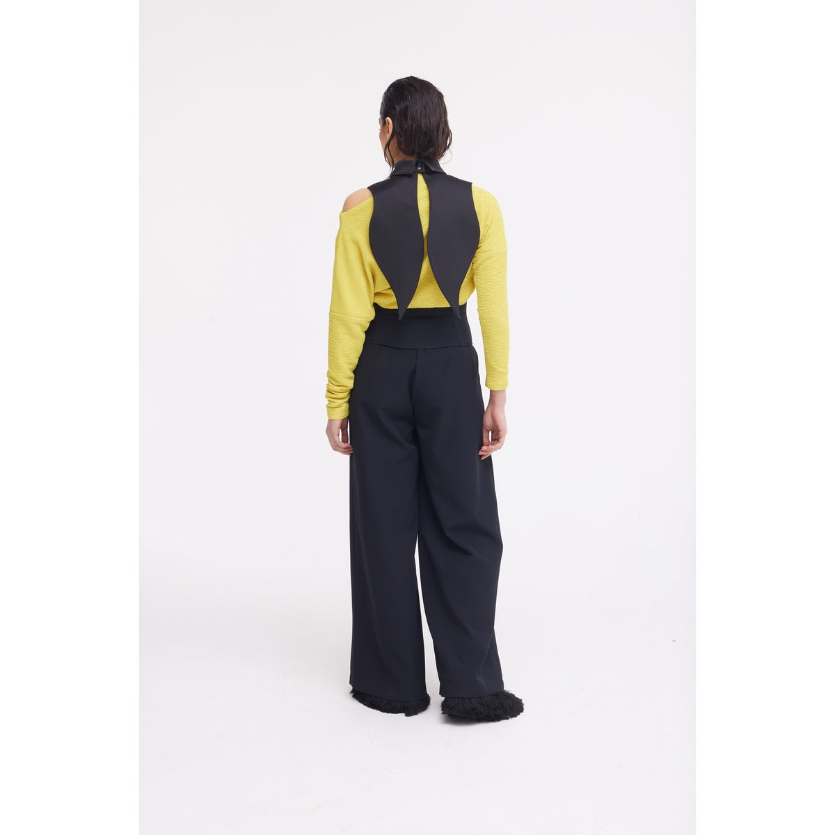 A person faces away in a yellow long-sleeve top with black shoulder cutouts and JULIA ALLERT’s Buttoned Corset-Waist Black Tailored Trousers, set against a plain white background.