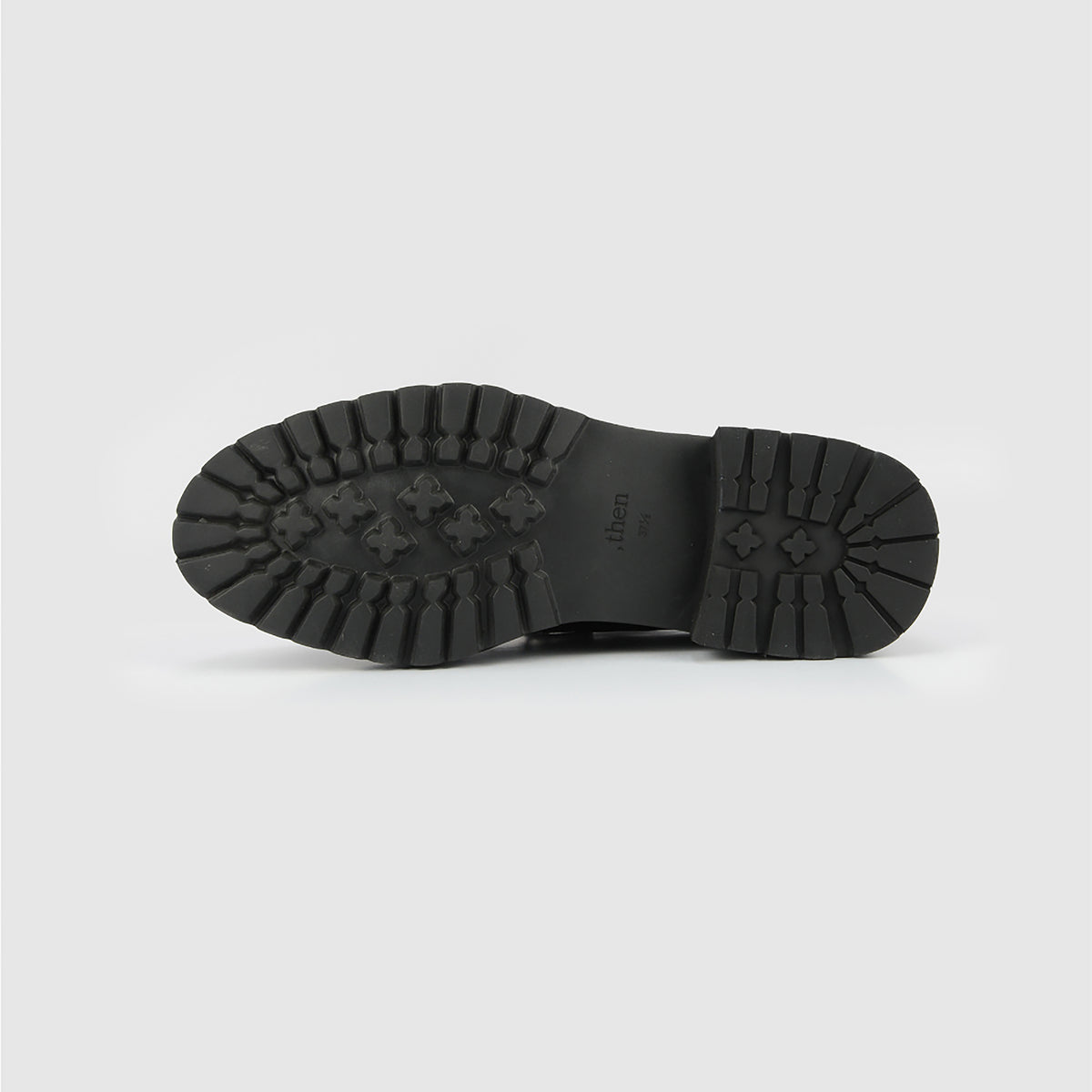 The image shows the black rubber lug sole of THEN Black Chunky Leather Derby Shoes, featuring a rugged tread pattern, photographed against a plain white background.