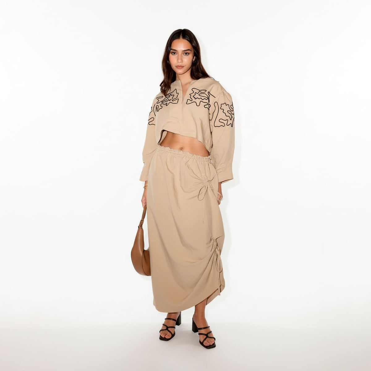 Woman wearing a beige outfit with intricate patterns on a white background