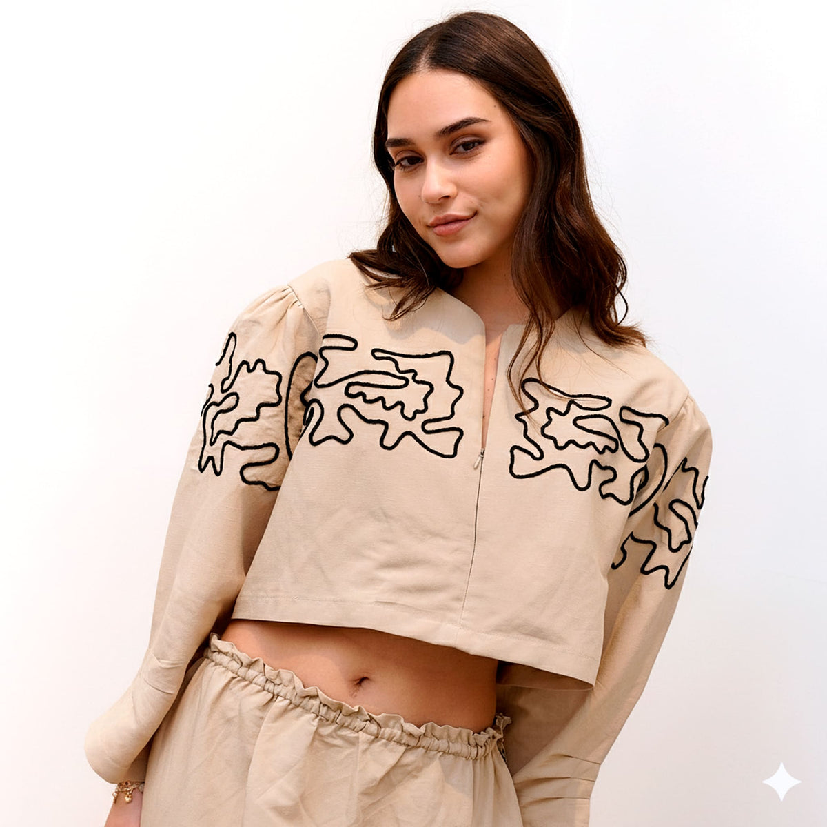 Woman wearing a beige jacket with black abstract patterns on a white background