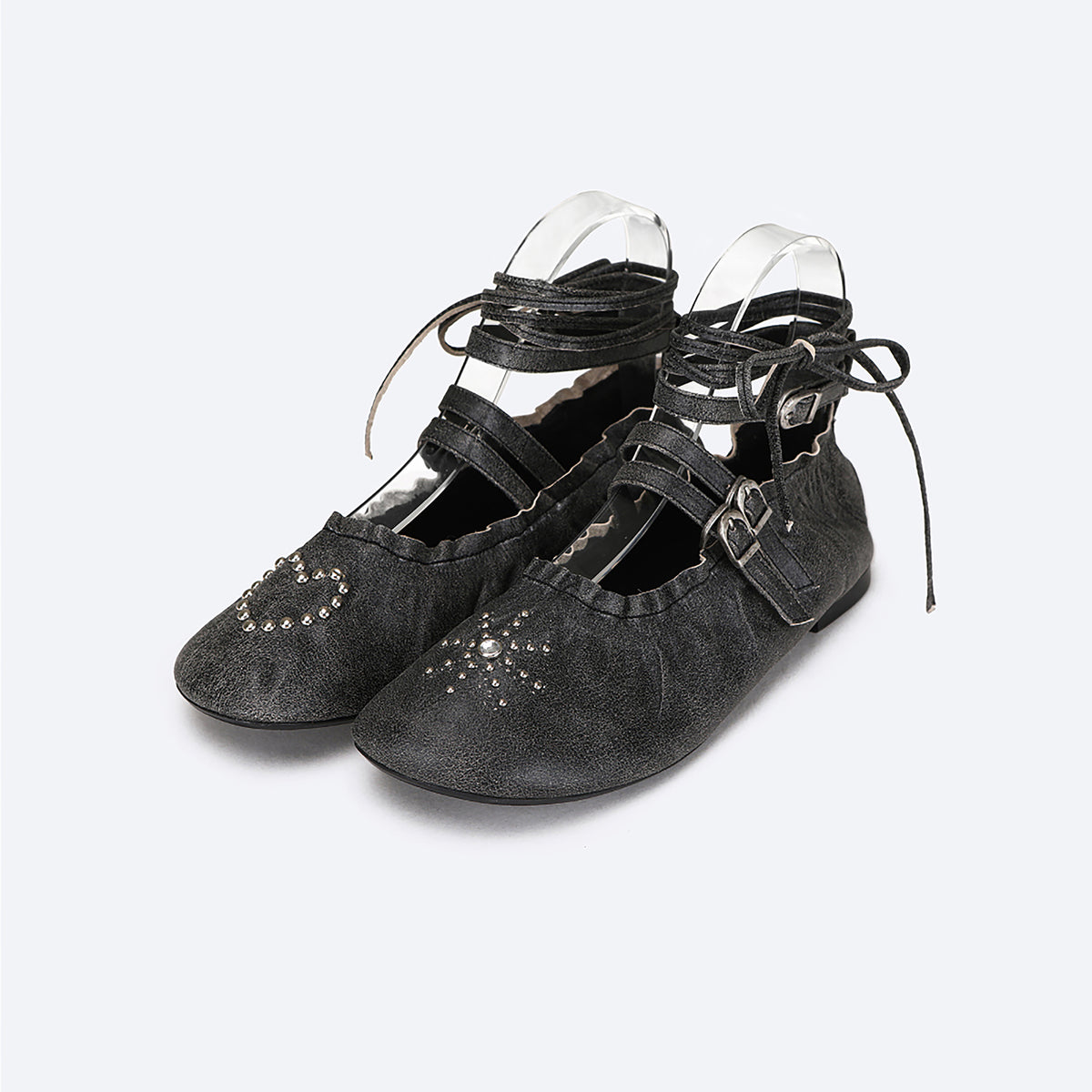 The THEN Black Distressed Lace-Up Ballerina Flats feature ankle straps, buckle closures, wraparound laces, and heart-shaped silver stud accents on the toes.
