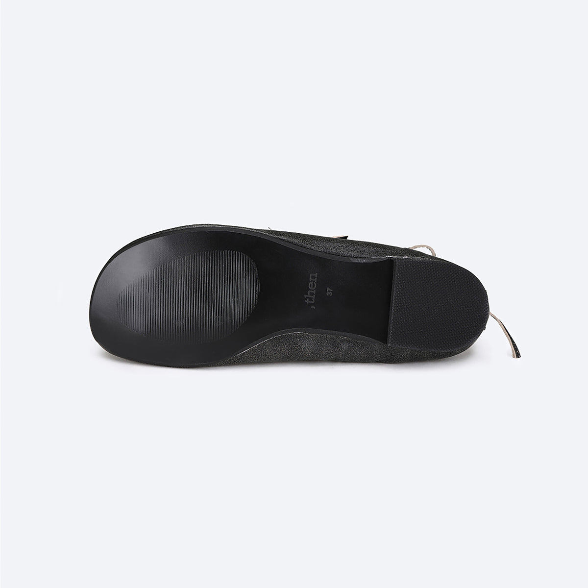 Flat-lay of the THEN Black Distressed Lace-Up Ballerina Flats shows the black rubber sole with textured grip, visible text, and wraparound laces peeking out on the right, set against a light grey background.