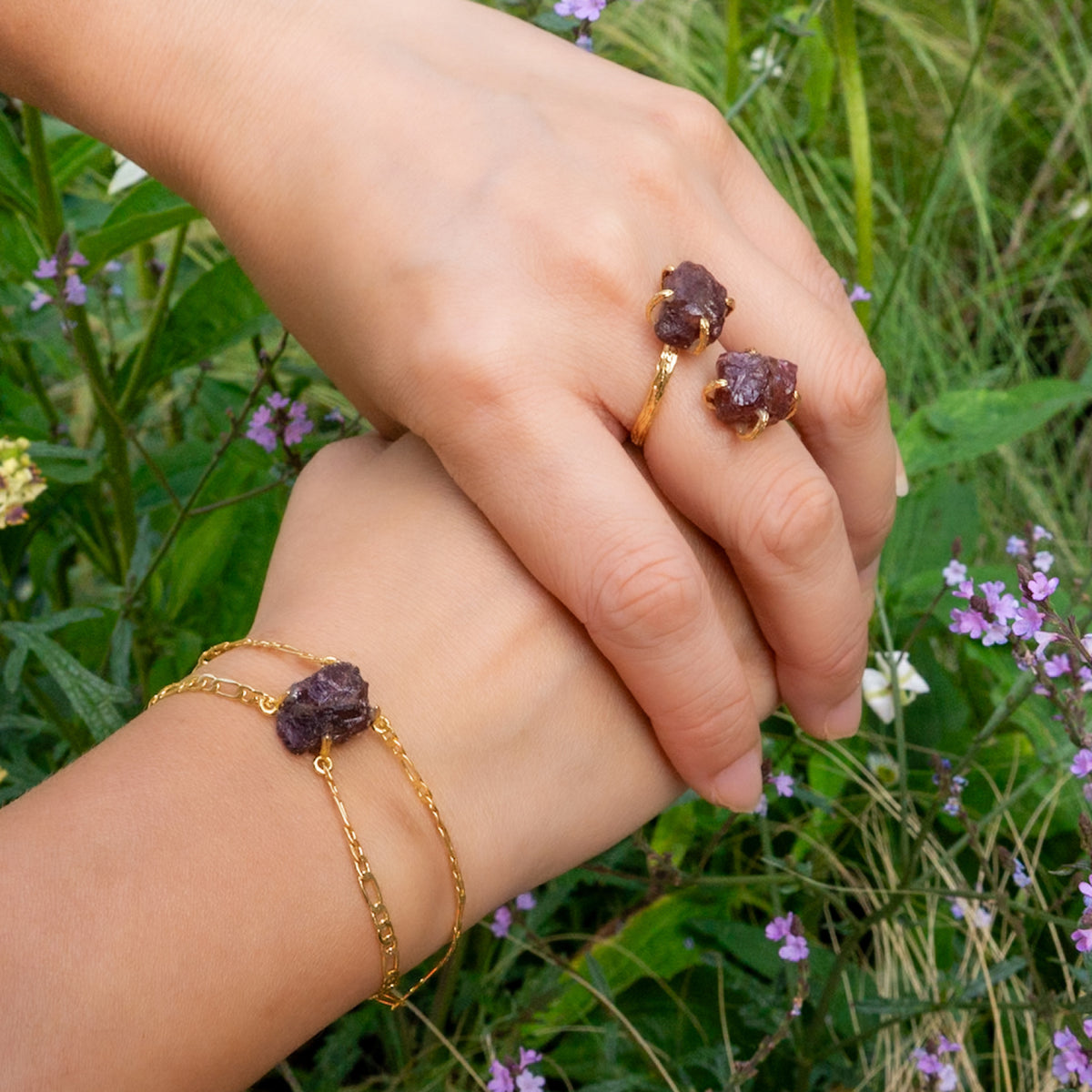 Two hands holding each other with gold rings and bracelet against a natural background