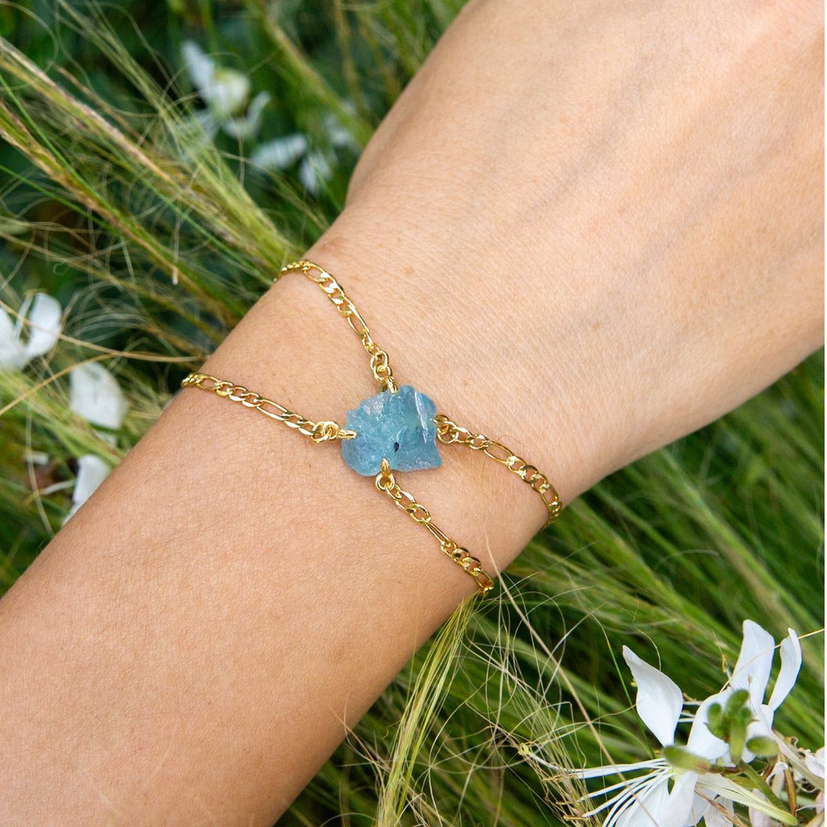 Gold bracelet with a blue stone on a wrist against a natural background