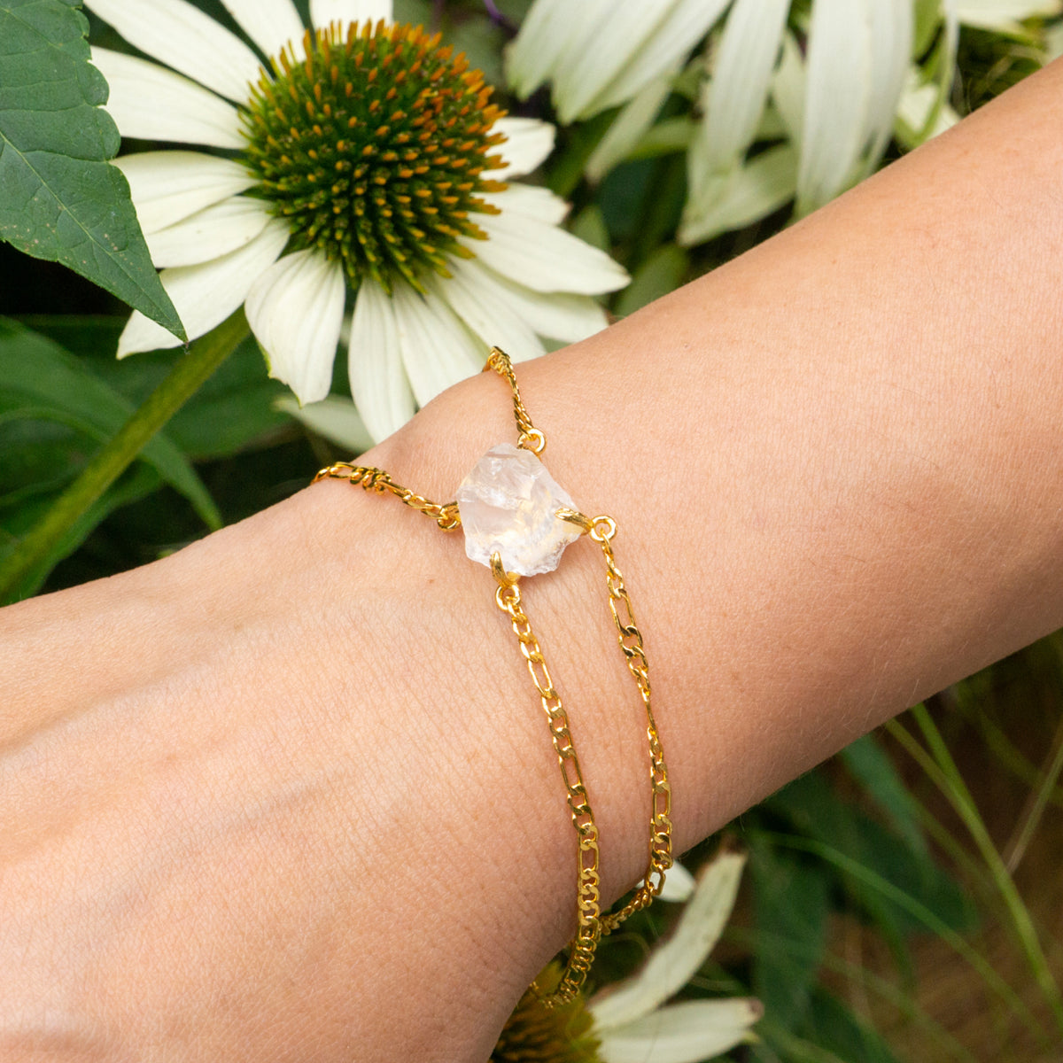 Gold bracelet with a clear stone on a wrist, with flowers in the background