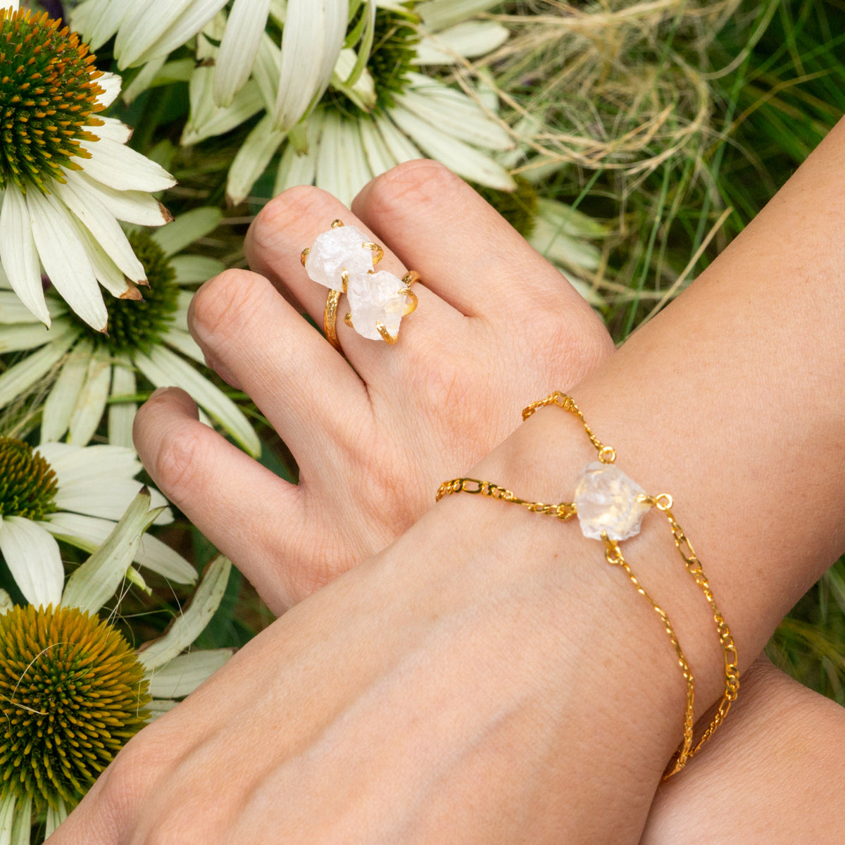 Gold bracelet and ring on a hand with flowers in the background