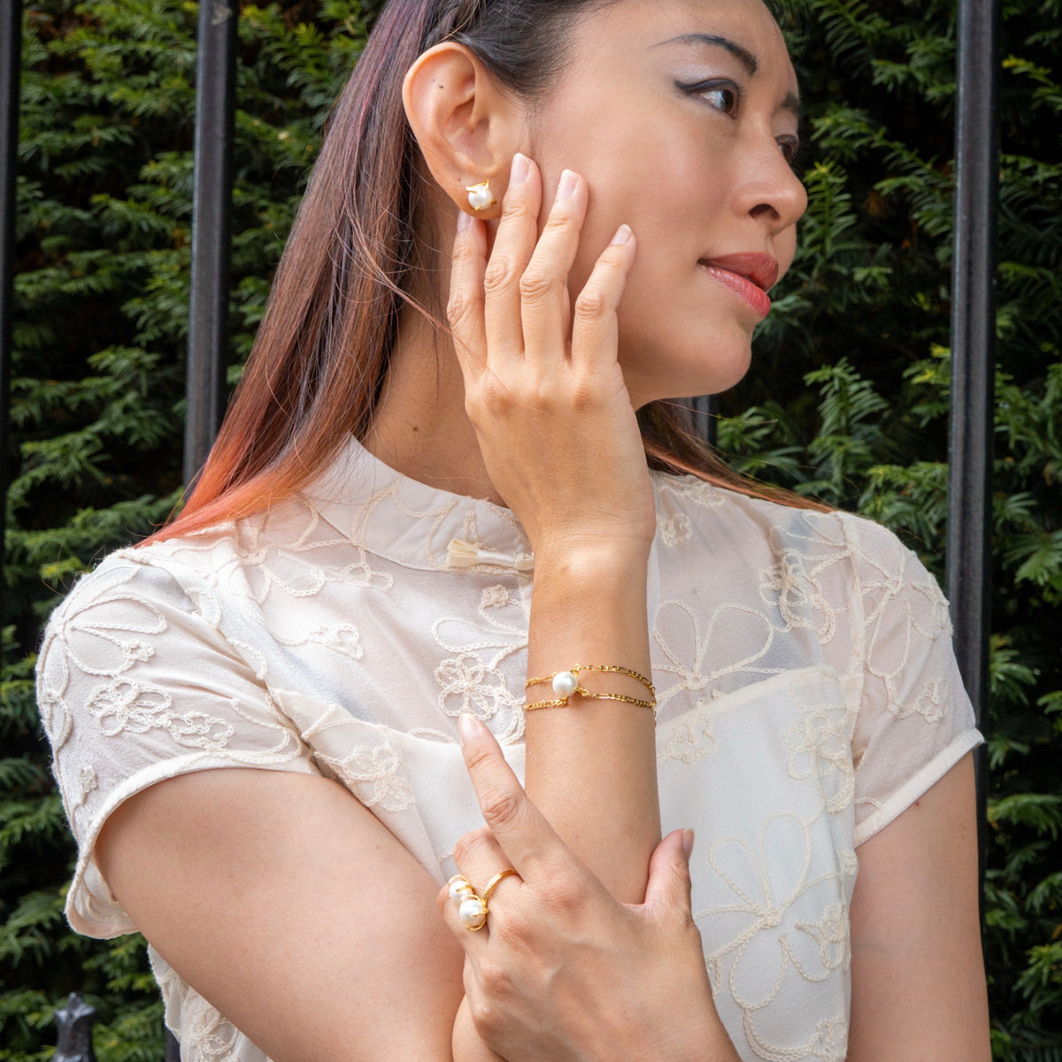 Woman wearing gold jewelry outdoors with greenery in the background