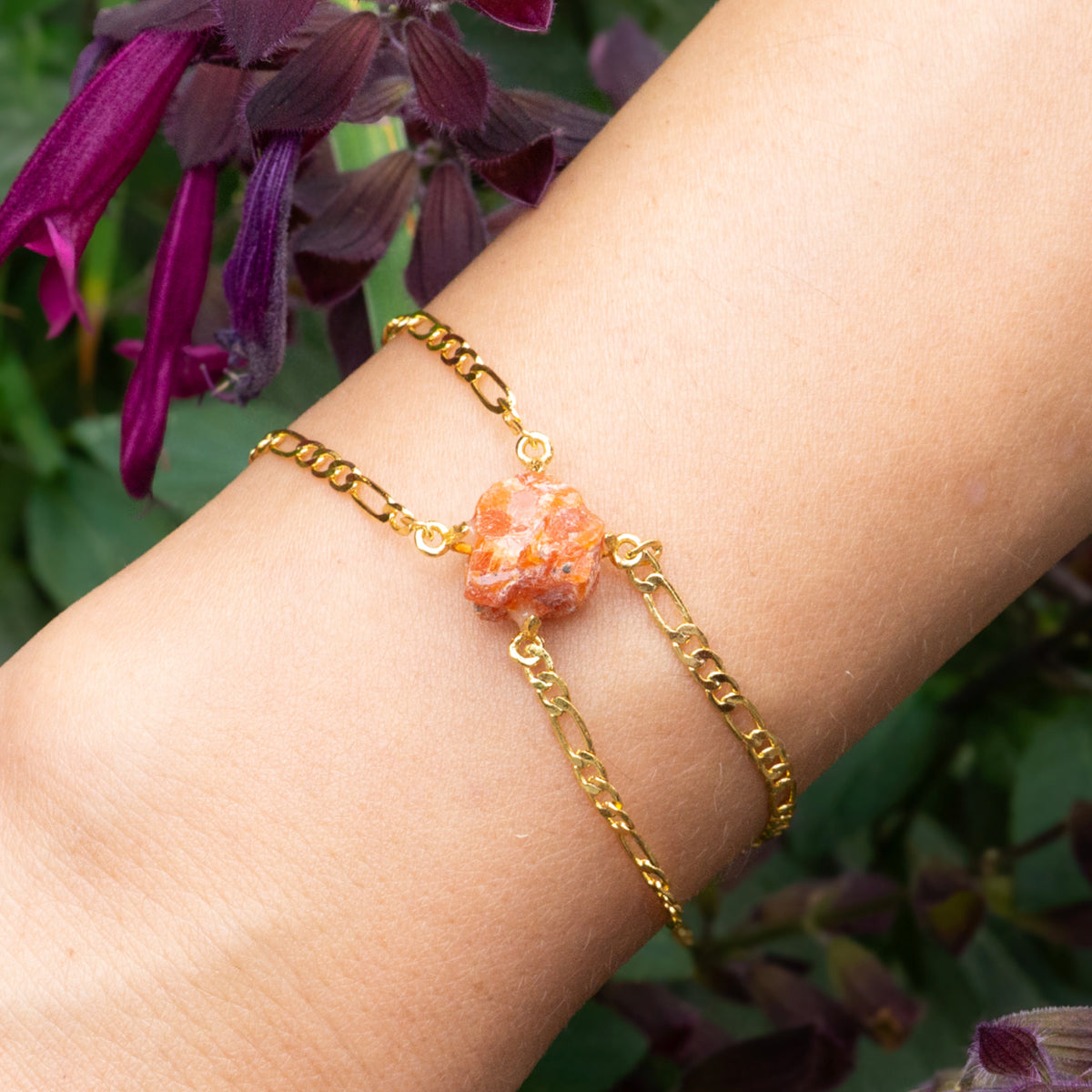Gold bracelet with a stone on a wrist against a blurred floral background