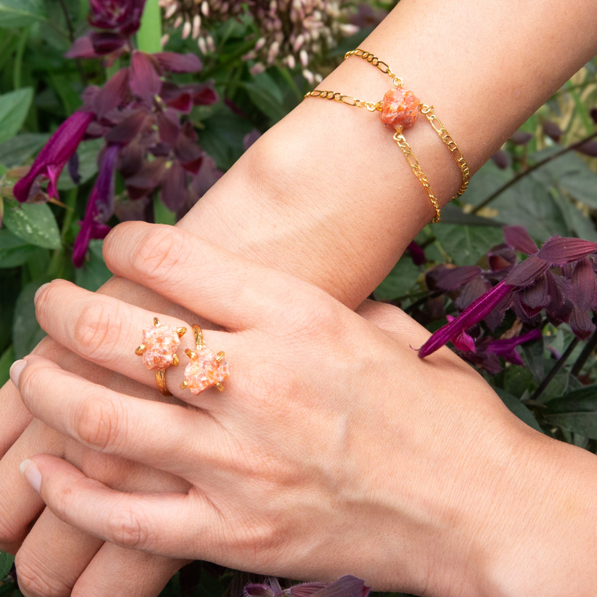 Close-up of hands wearing gold rings and bracelets with purple flowers in the background
