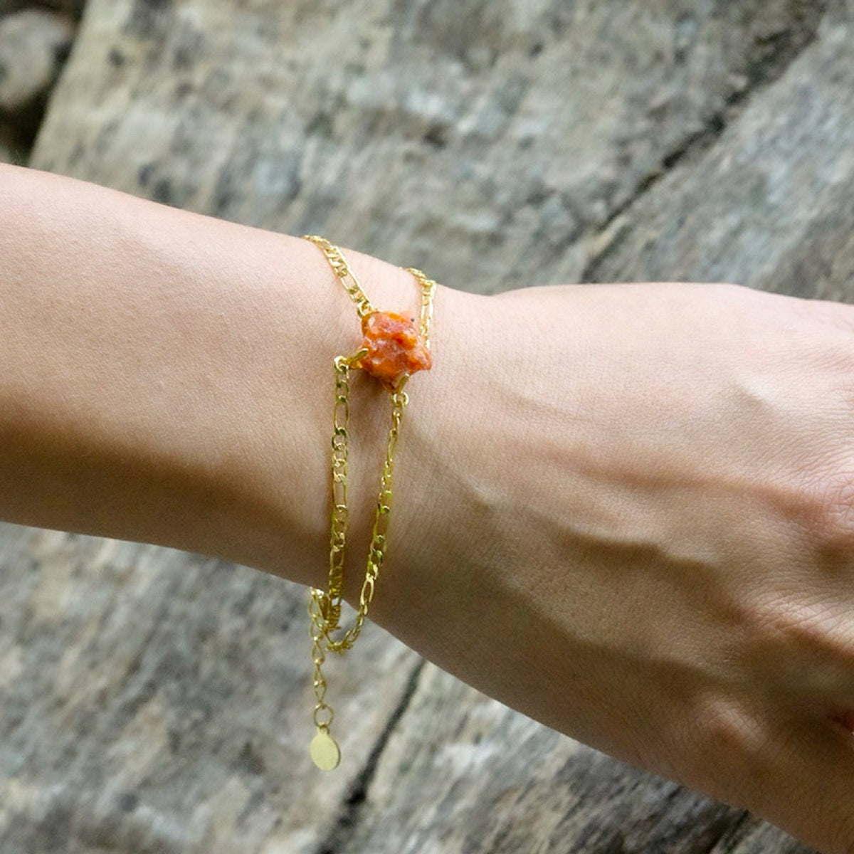 Gold bracelet with a red stone on a wrist against a wooden background