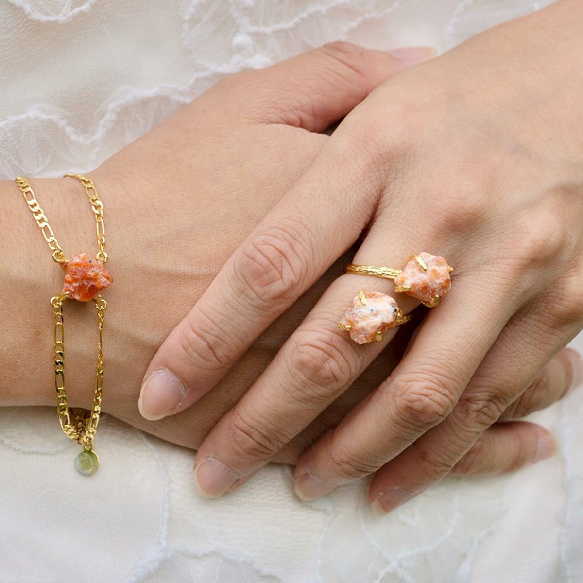 Close-up of hands wearing gold rings and a bracelet with coral-like stones on a light background
