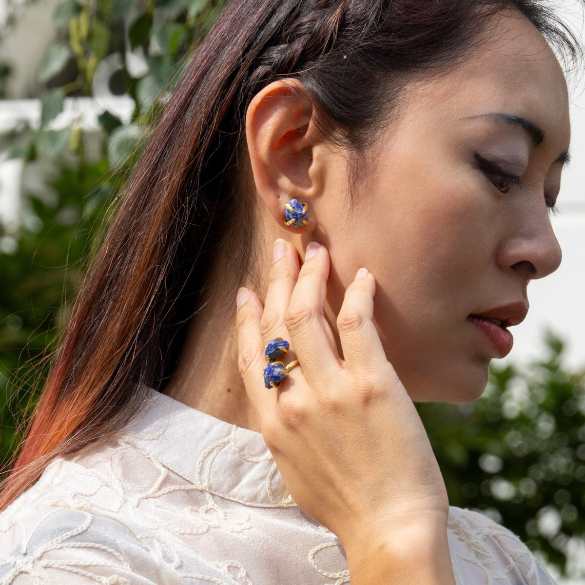 Woman wearing a ring and earrings outdoors with greenery in the background