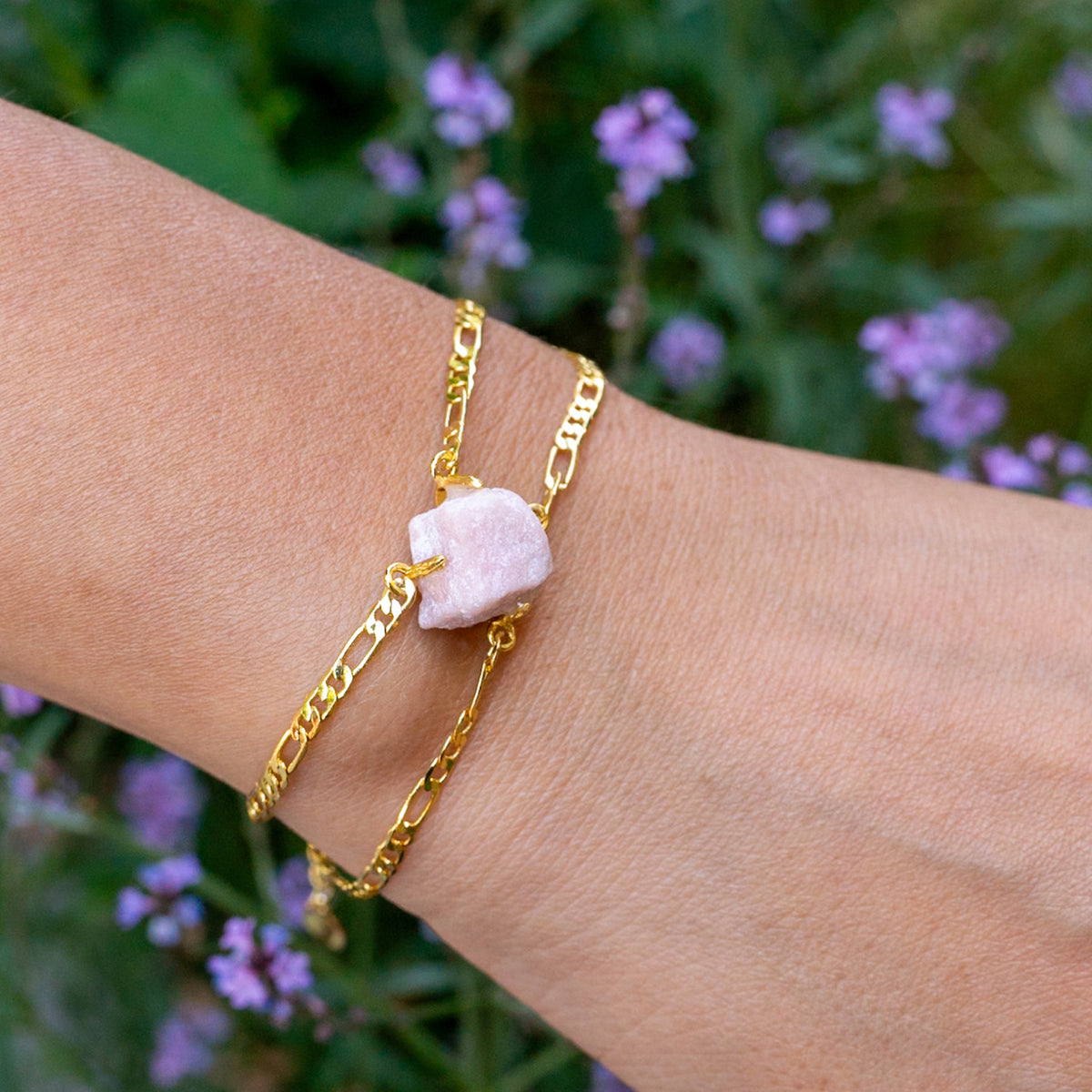 Gold chain bracelet with a pink stone on a wrist against a blurred natural background