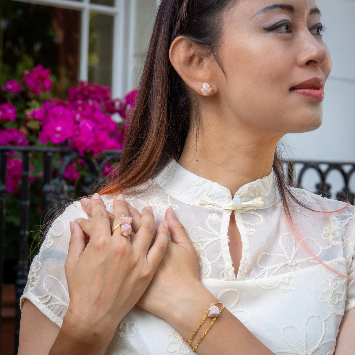 Woman wearing a white lace top with a bow, holding hands with another person outdoors.