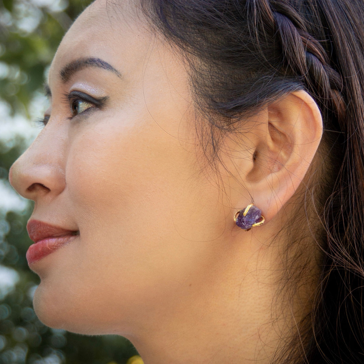 Close-up of a woman wearing a purple earring with a blurred natural background