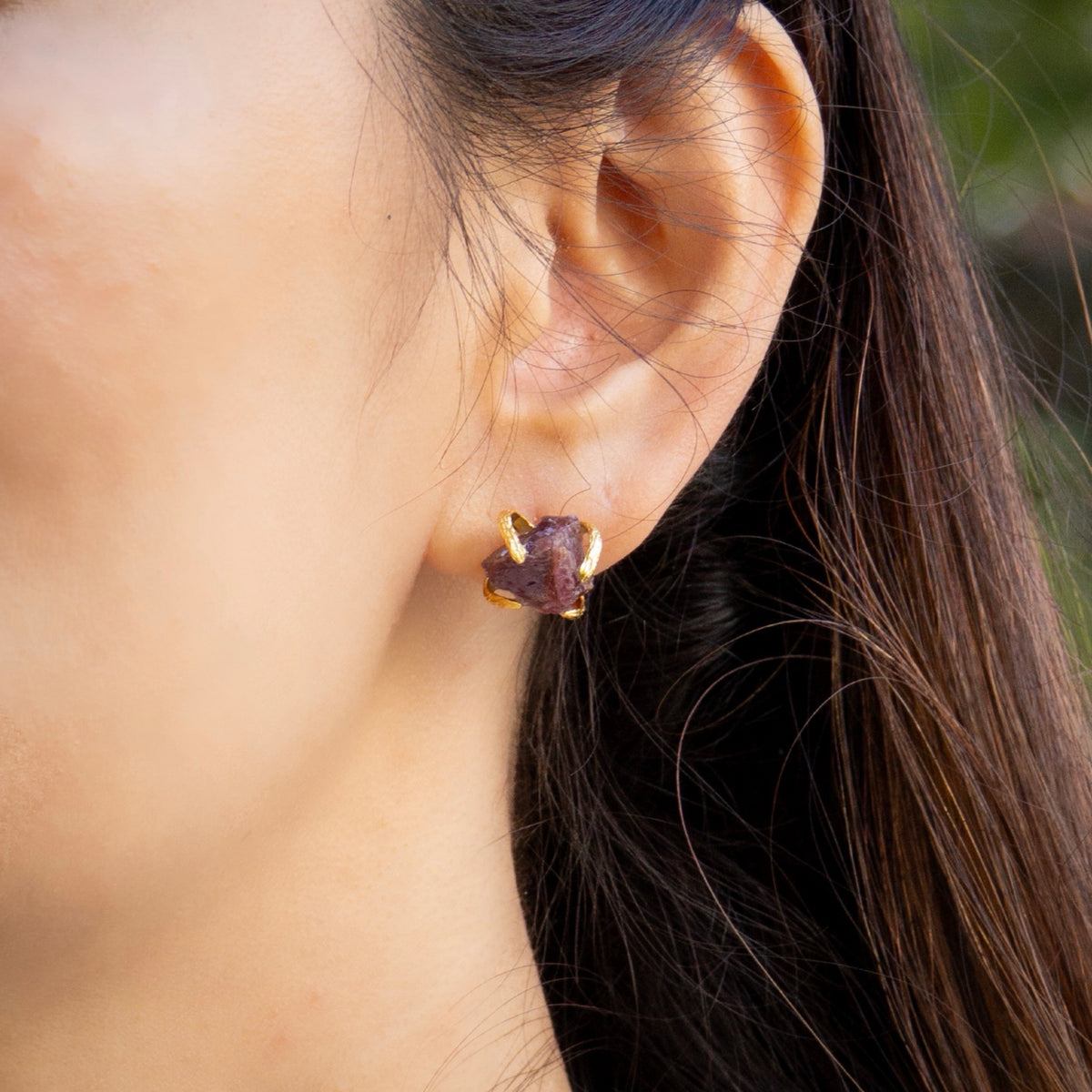 Close-up of an ear wearing a purple gemstone earring with gold setting.