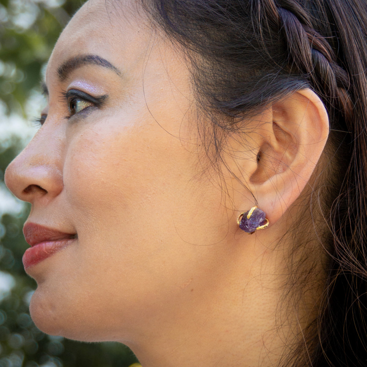 Close-up of a woman wearing purple earrings with a blurred natural background