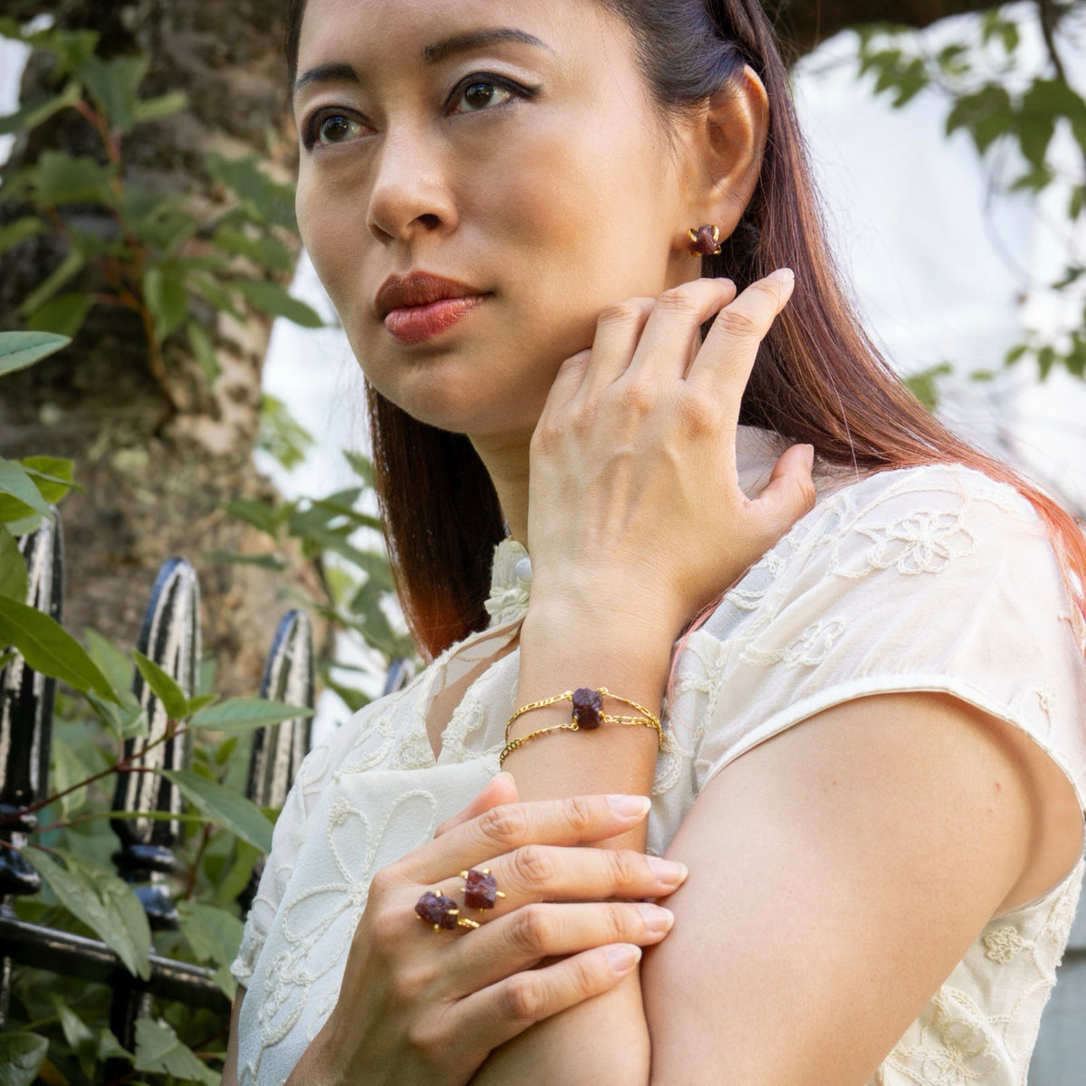 Woman wearing jewelry outdoors with greenery in the background