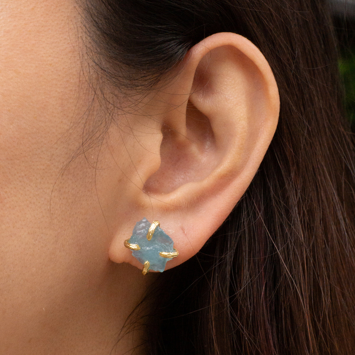 Close-up of an ear wearing a blue gemstone earring with gold accents.