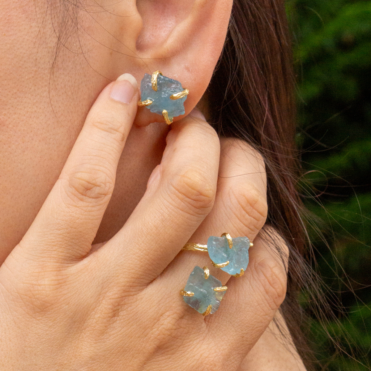 Close-up of a person wearing light blue gemstone earrings with gold accents.