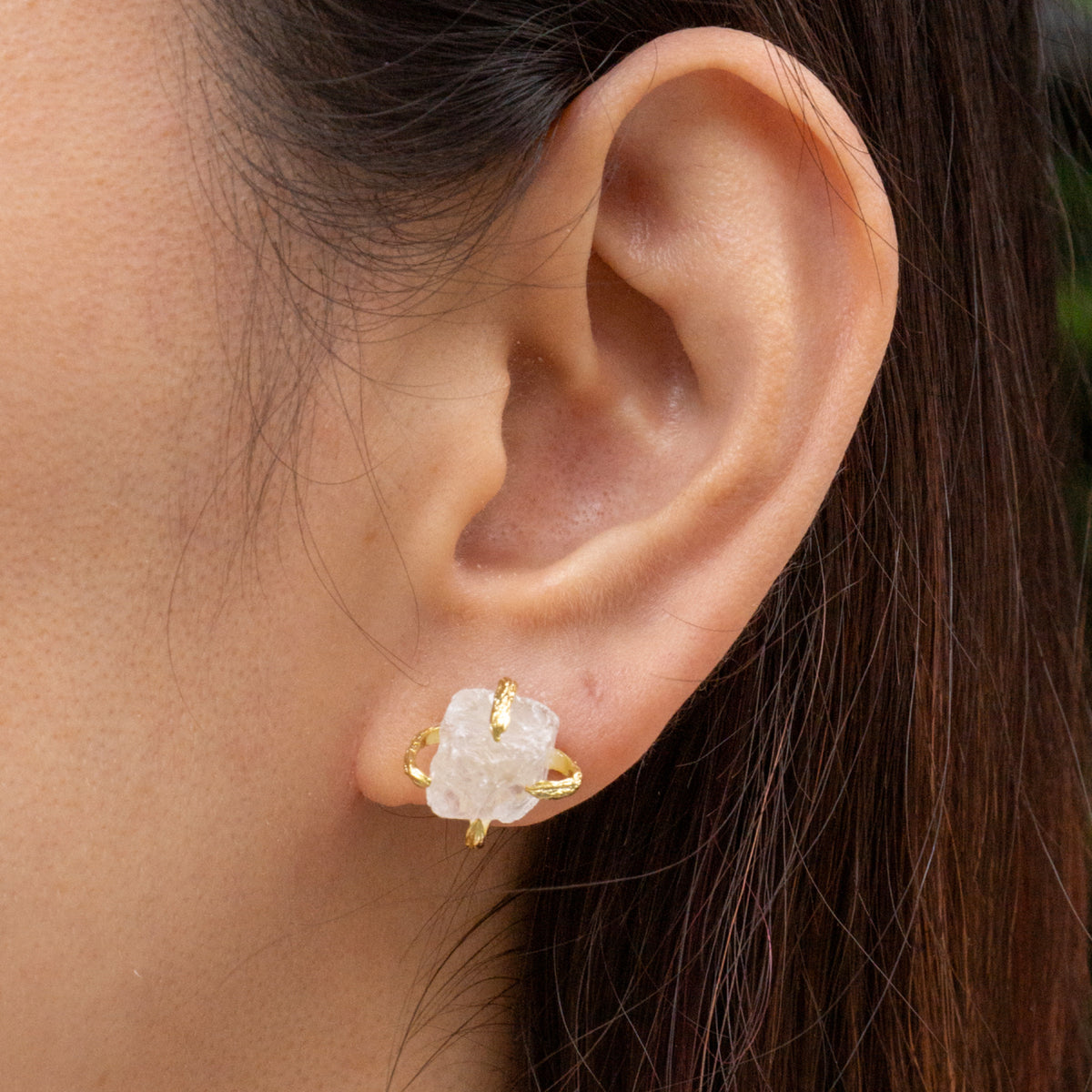 Close-up of an ear wearing a gold earring with a clear stone.