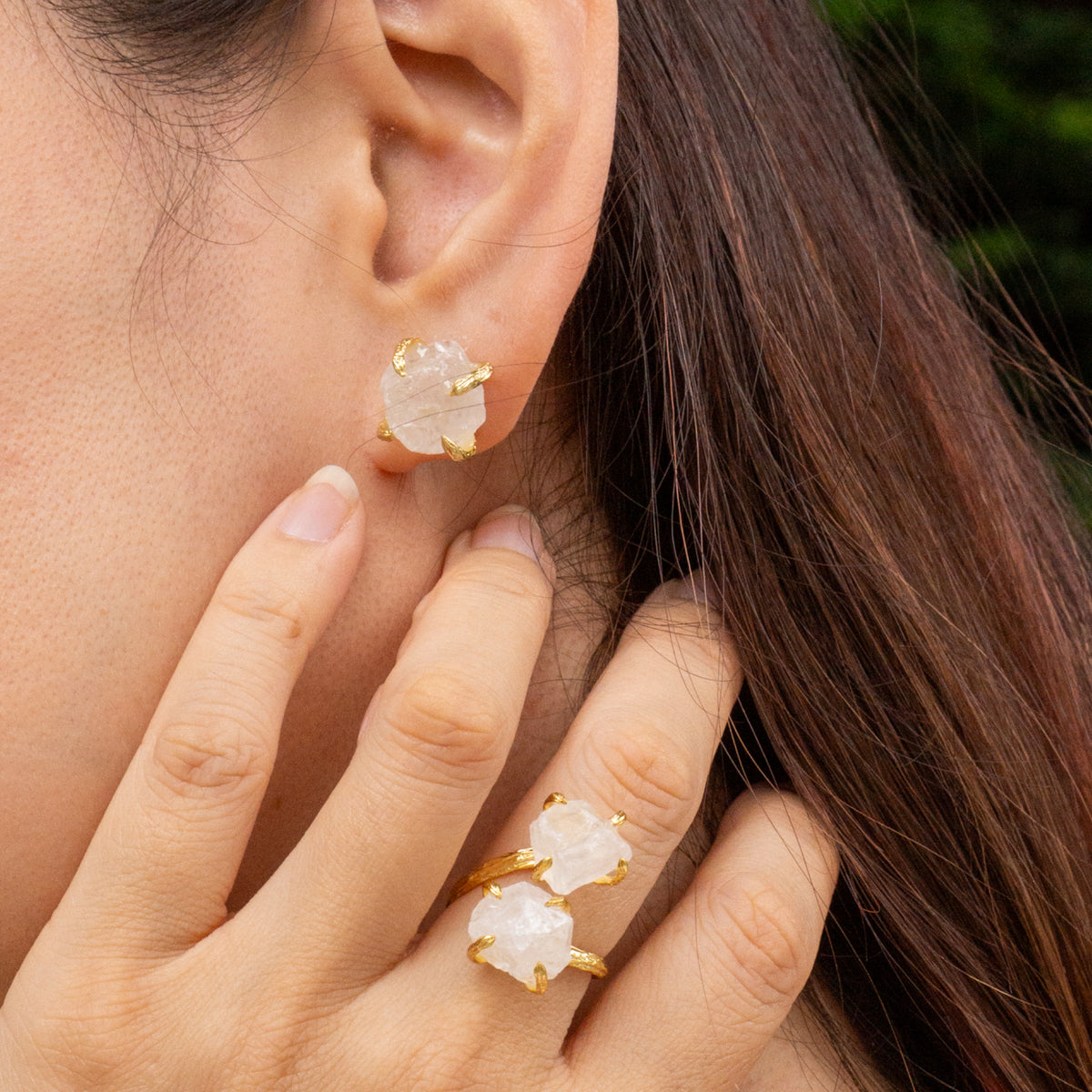 Close-up of a person wearing gold earrings and a ring with a pink stone.