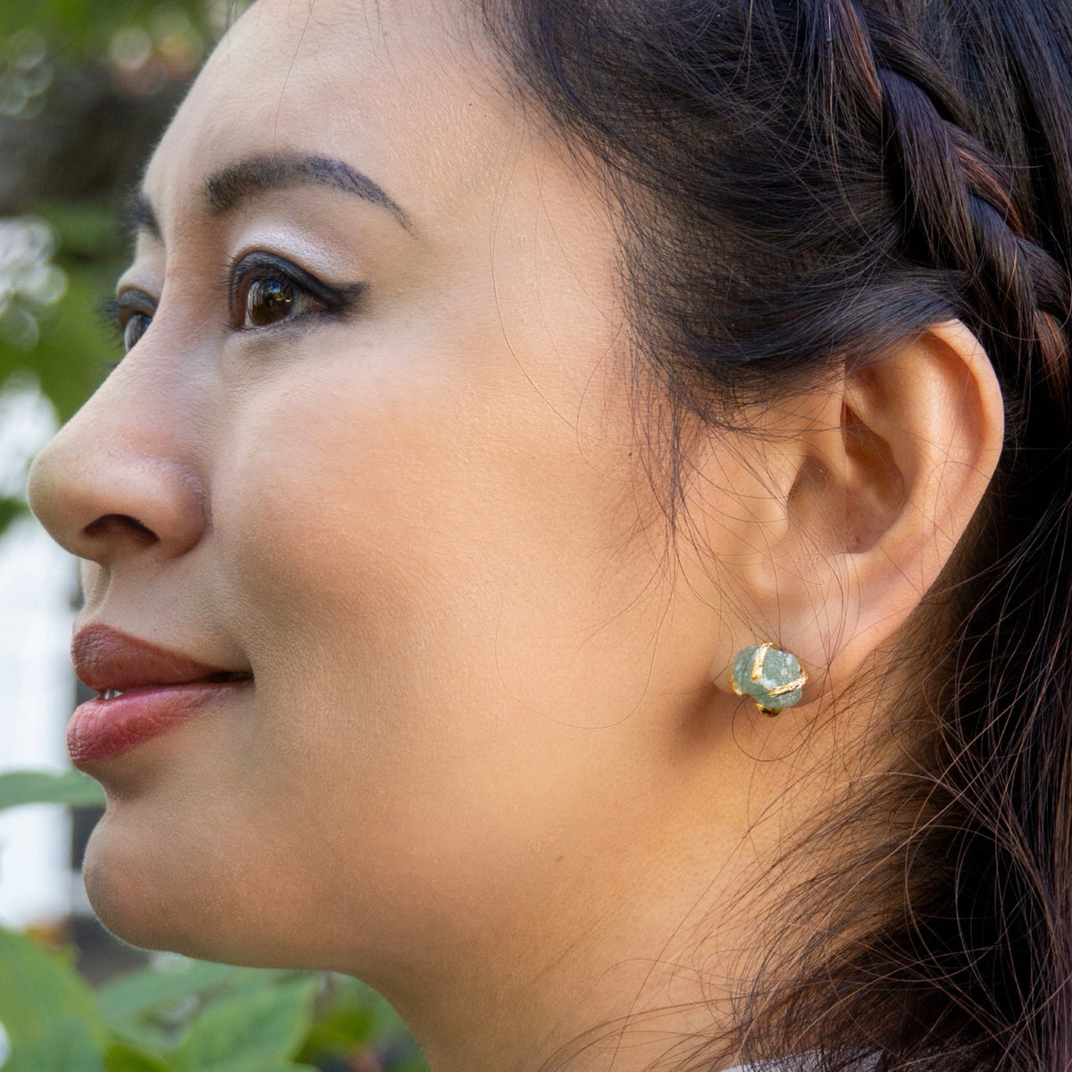 Close-up of a woman wearing a gold earring with a green gemstone, outdoors.