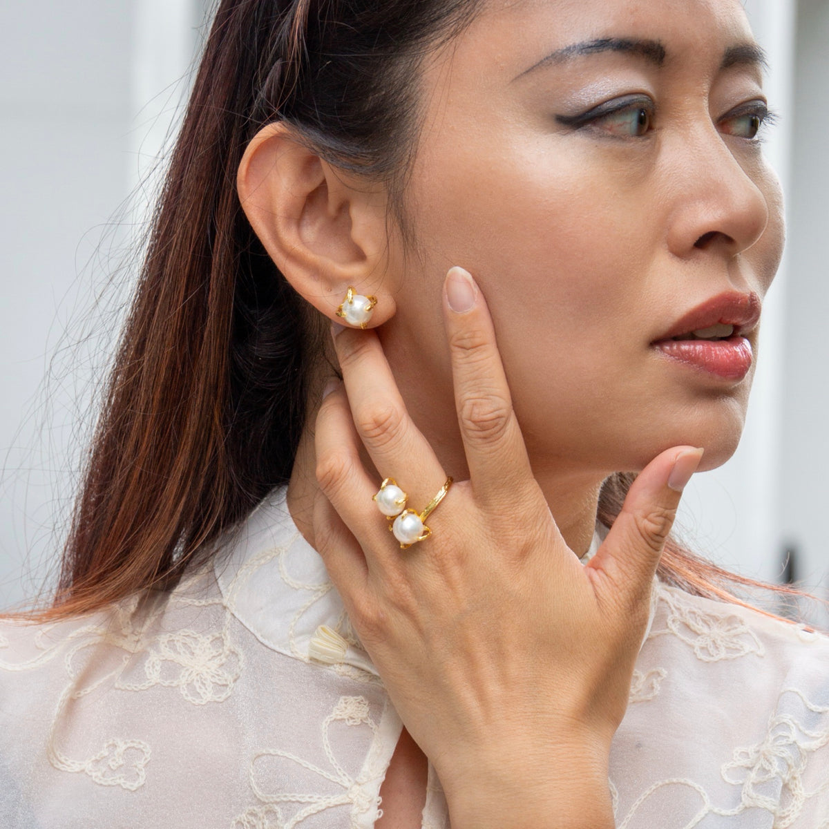Woman wearing pearl earrings and ring, close-up of face and hand.