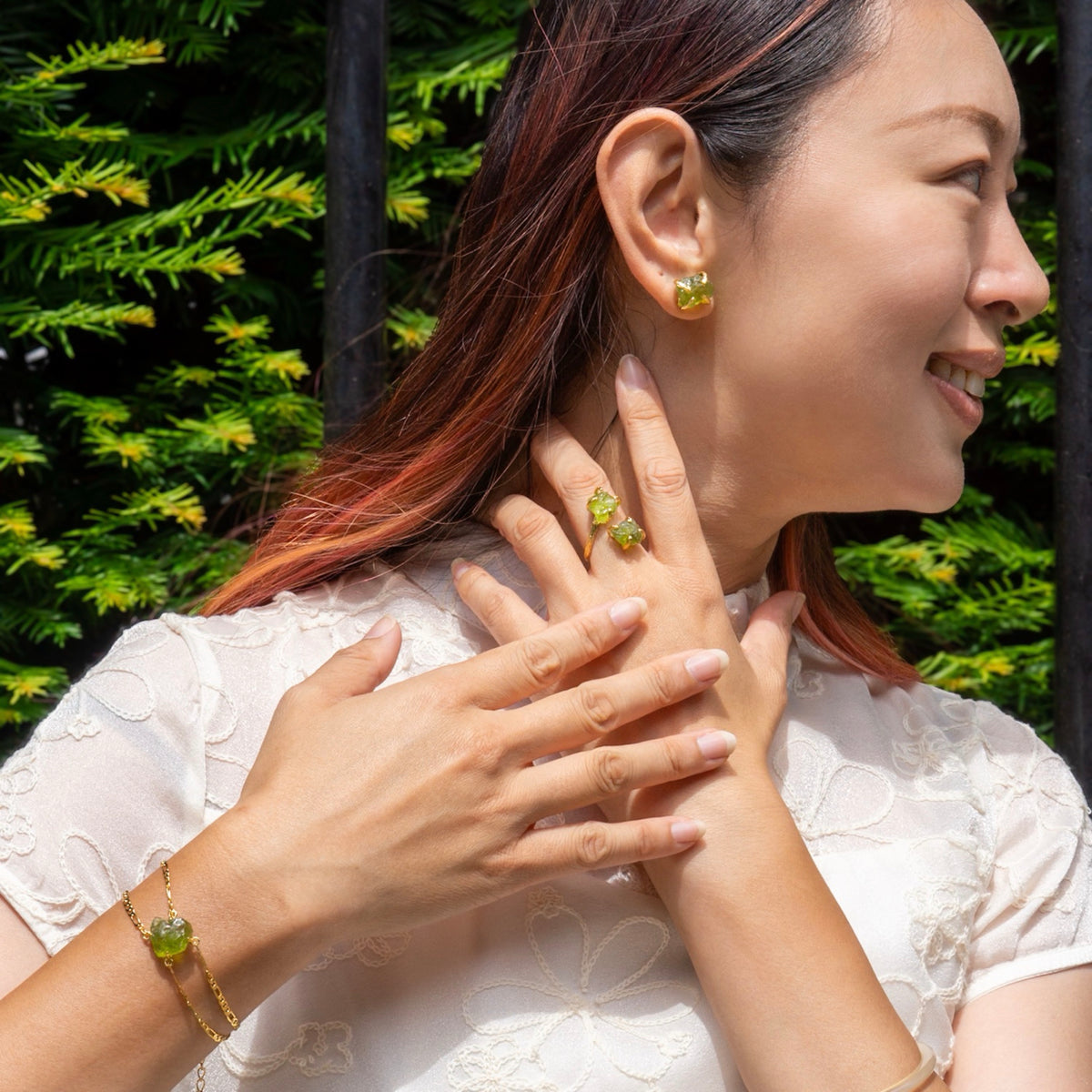 Woman wearing green gemstone earrings and bracelet against a blurred green background