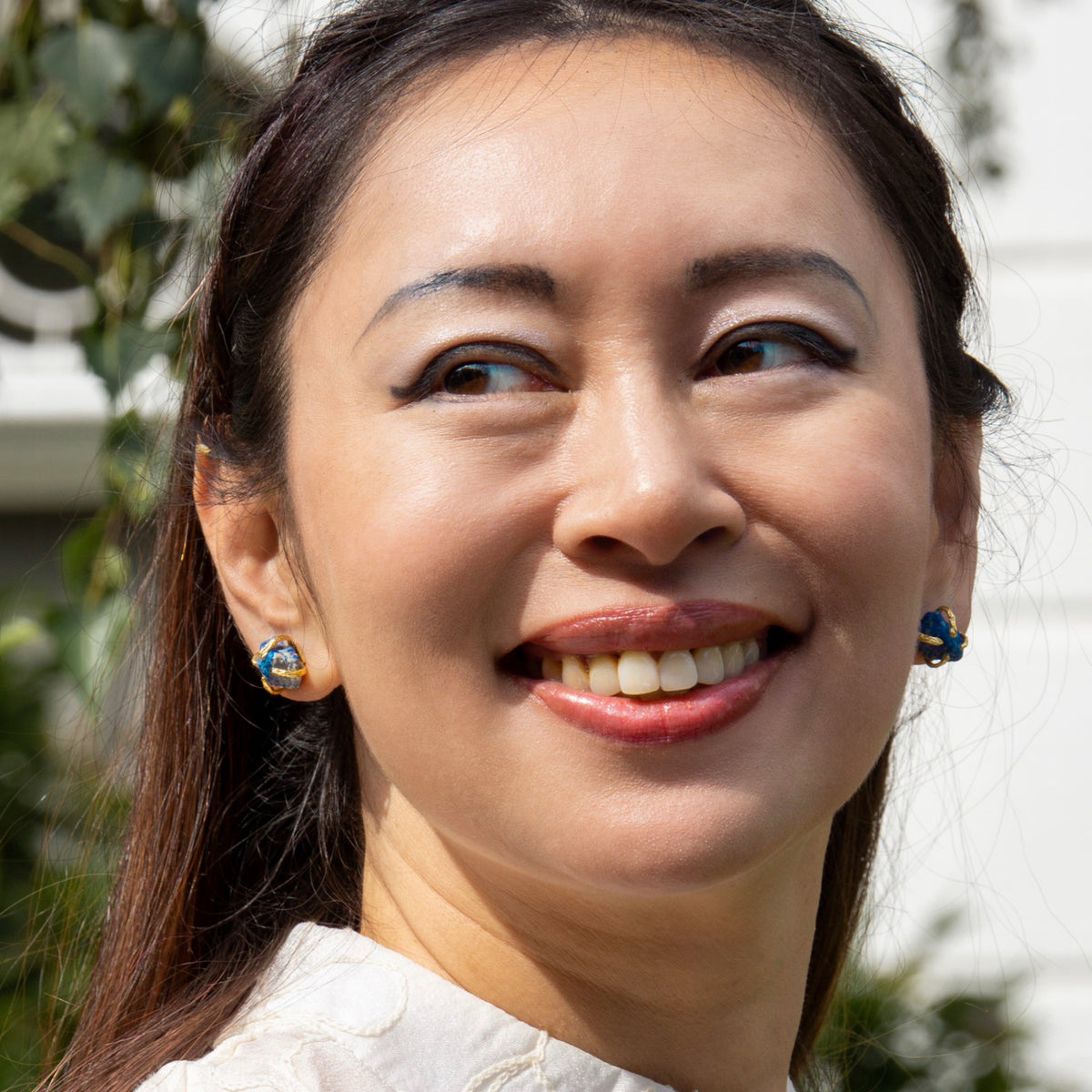 Woman with a smile, wearing earrings, outdoors with blurred background